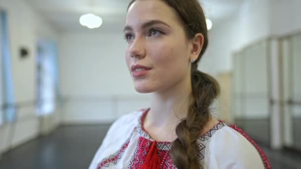 身穿民族服装的快乐迷人的乌克兰年轻女子站在室内，微笑着向远方望去。快乐美丽的白人舞蹈演员在室内的舞蹈演播室表演. — 图库视频影像