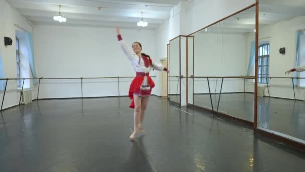 Amplia toma de delgada hermosa mujer joven ucraniana en traje nacional girando en cámara lenta ensayando danza en el estudio. Feliz hermosa bailarina caucásica realizando danza folclórica en interiores. — Vídeo de stock