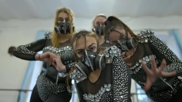 Vista inferior de bailarinas extravagantes en trajes modernos mirando a la cámara moviendo las manos bailando en cámara lenta. Cuatro mujeres caucásicas jóvenes ensayando actuación de moda en interiores en estudio de danza. — Vídeos de Stock