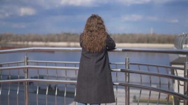 Doğanın güzelliğine hayran olan zarif, beyaz bir kadının arka planda duruşu. İnce, düşünceli esmer milenyum güneşi altında açık havada nehre bakıyor. Boş zaman ve yaşam tarzı.