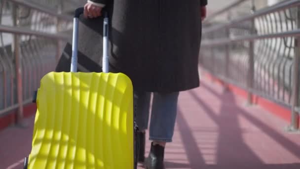 Live camera follows yellow travel bag as unrecognizable Caucasian young woman walking in slow motion along urban pedestrian bridge. Young confident millennial with luggage on sunny day outdoors. — 비디오