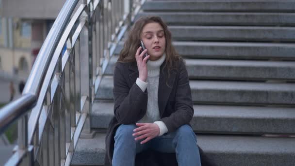 Angry furious young woman arguing talking on the phone in slow motion hanging up. Portrait of stressed Caucasian brunette beautiful millennial quarrelling on smartphone sitting on urban stairs. — ストック動画