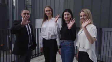 Group of positive business people waving smiling looking at camera. Four Caucasian man and women posing outdoors. Slow motion.
