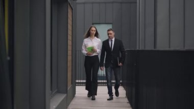 Wide shot serious Caucasian man and woman walking for a meeting talking outdoors. Portrait of confident professional successful colleagues discussing business strolling in slow motion.