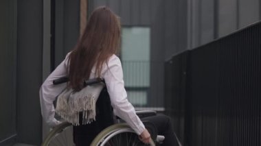 Young paraplegic woman rolling wheelchair outdoors leaving. Portrait of slim beautiful disabled Caucasian elegant businesswoman riding away in slow motion. Disability and business concept.