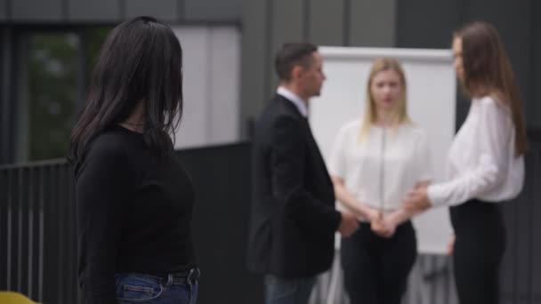 Caucasian woman closing ears with hands looking at camera as nervous colleagues arguing at background. Portrait of stressed employee posing outdoors with coworkers quarrelling. Inconvenience concept. — Vídeo de Stock