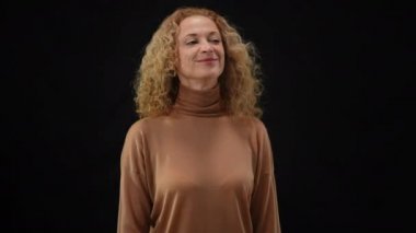 Siyah arka planda duran kendine güvenen, gülümseyen bir kadının kamera flaşlarıyla etrafa bakındığı orta ölçekli bir fotoğraf. Basın toplantısında gazetecileri ve paparazzileri selamlayan kadın portresi.