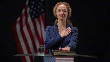 Güvenilir seçilmiş politikacı kadın el ele tutuşup milli marşı dinlerken kameraya bakıyor. Amerikan bayrağıyla siyah arka planda yemin eden başarılı kadının portresi..