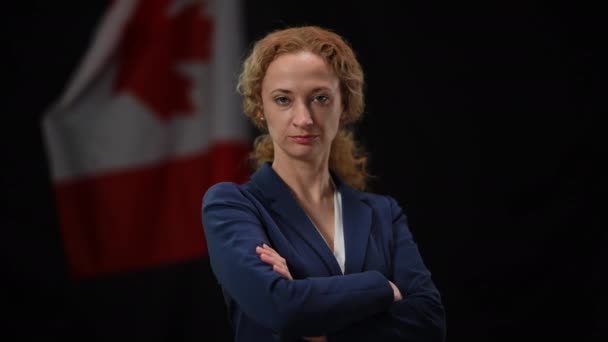 Уверенная в себе серьезная канадская женщина-политик обращается к камере, скрещивая руки. Портрет успешной умной дамы, позирующей на черном фоне с национальным флагом. Концепция доверия и политики. — стоковое видео