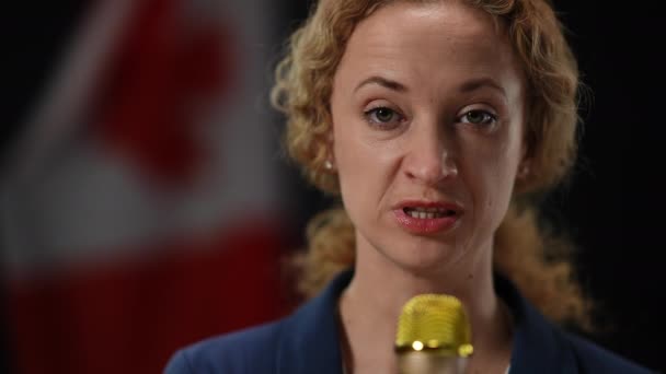 Close-up of confident journalist speaking in microphone at black background with Canadian flag. Portrait of serious elegant reporter talking telling news looking at camera. — Stock Video