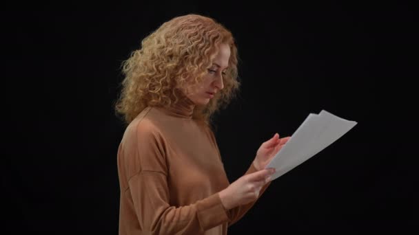 Gergin, beyaz bir kadın siyah arka planda konuşma provası yapmak için evrakları atıyor. Endişeli, sorunlu bir sözcünün el ele tutuşup bakışlarının yan görünümü.. — Stok video