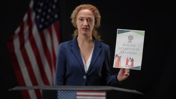 American politician woman activist holding Racial sensitivity training sign talking looking at camera. portrait of elegant slim lady presenting campaign at black background with national flag. — Stock Video