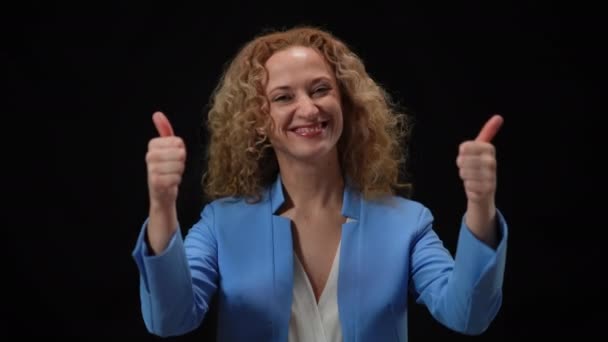 Šťastná žena ukazuje palce nahoru pózující v záblescích kamer na černém pozadí. Portrét usměvavého sebevědomého bělošského elegantního politika, který se dívá na gestikulaci kamery. Koncept úspěchu. — Stock video