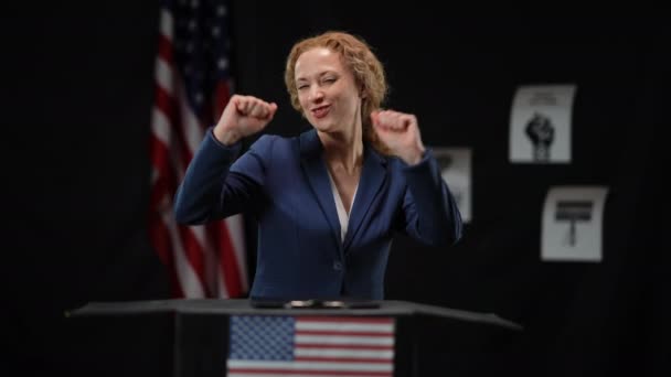 Vrolijke politicus vrouw dansend glimlachend naar tribune verheugende overwinning op de verkiezingen. Portret van een opgewonden elegante dame met Amerikaanse vlag op zwarte achtergrond. Vreugde en succes in de politiek. — Stockvideo