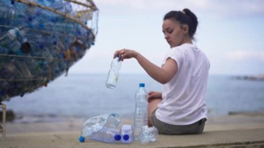 Plajda oturup plastik şişe bırakan genç turistin arkası. Sorumsuz beyaz kadın tatillerde doğayı kirletiyor. Ekoloji ve kirlilik kavramı.