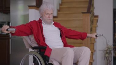 Kendinden emin, sakat, tekerlekli sandalyedeki yakışıklı adam ağır çekimde dambılları kaldırıyor. Motive olmuş Kafkas engelli emeklilik eğitiminin portresi. Spor ve sakatlık.