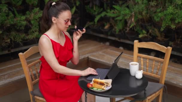 Professional freelancer talking on speakerphone typing on tablet keyboard sitting in cafe outdoors in sunlight. Portrait of beautiful Caucasian young woman working online in slow motion. — ストック動画