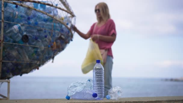 Suddig kvinna sätta plastavfall på särskild plats på stranden kusten som oigenkännlig tusenårig passerar på framsidan lämnar tom flaska åt sidan. Livsstils- och miljökoncept. — Stockvideo