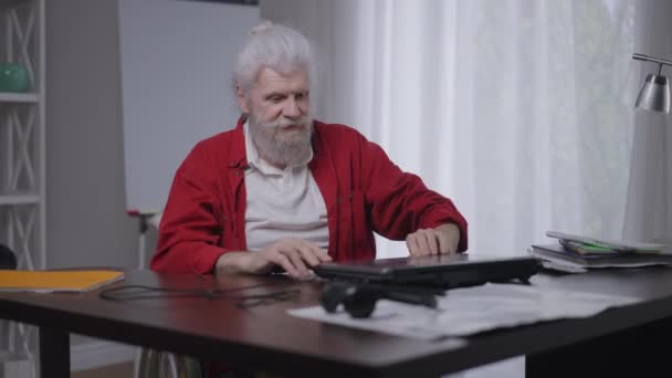 Senior bearded Caucasian disabled man closing laptop rolling wheelchair to window in home office. Portrait of confident handicapped freelancer having break working online. Slow motion. — 图库视频影像