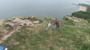 Babasının küçük kızını uçurumun kenarında döndürdüğü ve dışarıda eğlendiği hava aracı görüntüsü. Geniş açılı mutlu beyaz adam ve kız yaz günlerinde seyahat ediyorlar..