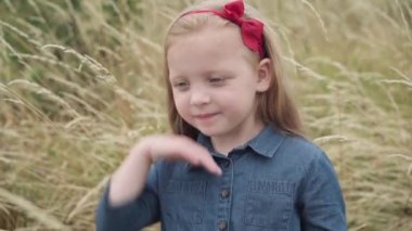 Sarışın kırmızı kurdeleli sevimli küçük kız sonbahar tarlasında dikilirken gözlerini kaçırıyor. Kafkasyalı güzel bir çocuğun boş zamanlarında çekilmiş portresi. Çocukluk ve doğa kavramı.