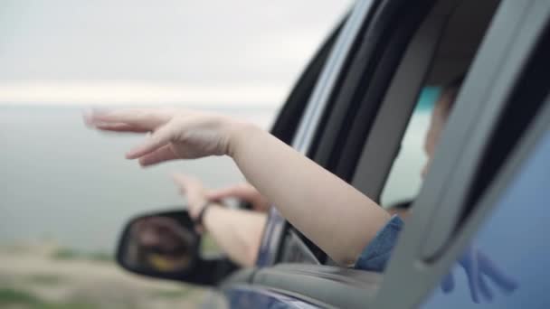 Close-up little female hand sticking out car window with blurred male Caucasian arm at background. Unrecognizable daughter and father enjoying road trip in car on river bank outdoors. — Stock Video