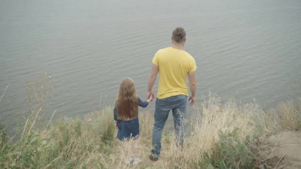 Široký pohled na mladého muže a holčičku stojící na útesu nad řekou, jak si povídají a gestikulují. Šťastný uvolněný bezstarostný Kavkazský otec a dcera obdivující krásu přírody cestování venku. — Stock video