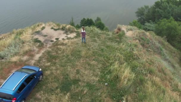 Pequena menina caucasiana com cabelos longos sentados nos ombros do homem em pé no penhasco sobre o rio nas montanhas. Amplo tiro de filha e pai admirando a natureza ao ar livre. Câmera ao vivo zoom out. — Vídeo de Stock