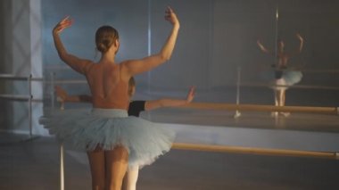 Kendine güvenen bale öğretmeni ve ilham verici öğrencinin dans stüdyosundaki aynada yansımaya bakışları. Motive olmuş kız içeride genç bir kadınla balo dansı öğreniyor..