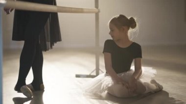 Büyüleyici beyaz kız profesyonel balerinin bacaklarını hayranlıkla seyrediyor. Sis ışıkları altında bale barında ilerlerken geleceği hayal ediyor. Balo salonundaki ilham verici çocuğun portresi. Yavaş çekim.