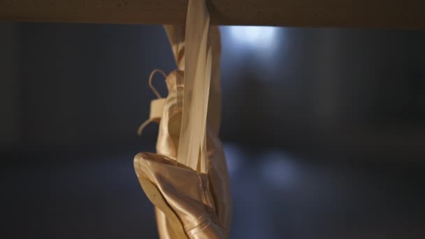 Zapatillas de punta dorada beige de primer plano colgadas en la barra de ballet en niebla retroiluminada. Puntas para el baile de salón en el estudio interior. Coreografía concepto de arte. — Vídeo de stock