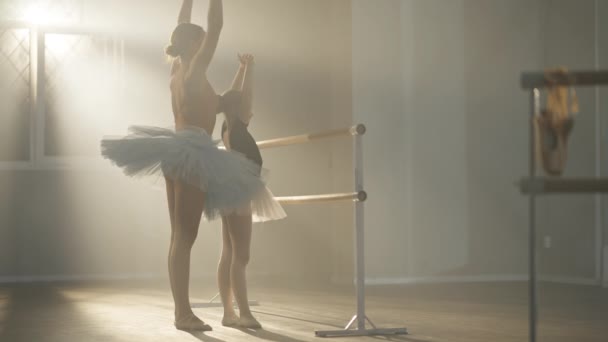 Учитель балета Кавказа объясняет движение рук талантливой девушке в танцевальной студии в тумане с подсветкой. Широкий снимок уверенной в себе балерины, беседующей со студенткой, преподающей бальные танцы в замедленной съемке. — стоковое видео