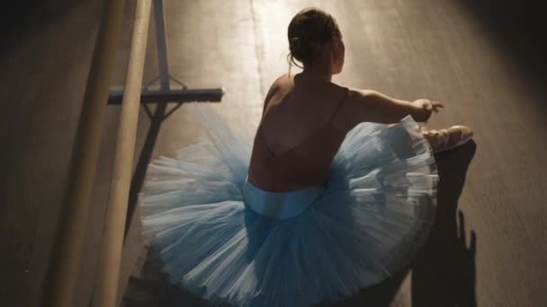 Yüksek açılı, ince yetenekli, çalışkan, mavi etekli balerin bej noktalı bağcıkları içeride bağlıyor. Muhteşem zarif beyaz kadın dans stüdyosunda provaya hazırlanıyor.. — Stok video