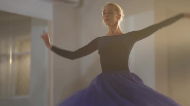 Camera moves down as slim elegant ballerina spinning on tiptoes in slow motion in backlit. Slender Caucasian beautiful woman dancing rehearsing performance in foggy studio indoors. — Stockvideo