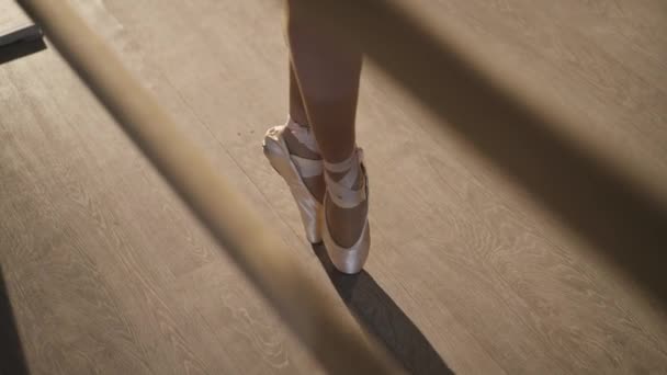 Vista de ángulo alto de las piernas delgadas femeninas en puntas beige en puntas de los pies haciendo pasos. Mujer caucásica esbelta irreconocible ensayando en la barra en el estudio de baile con retroiluminación. Arte y estilo de vida. — Vídeo de stock