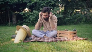Mutlu erkek çiftçinin geniş açılı portresi kulaklık takıp müzik dinleyerek mahsul topluyor. Kafkasyalı rahat yakışıklı genç adam saman şapkalı kabaklı çayırda oturuyor..