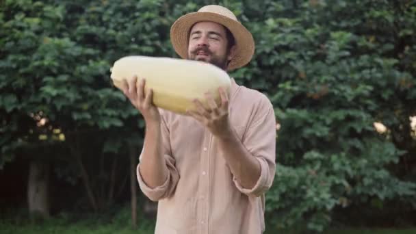 Medium skott porträtt av leende nöjd manlig bonde jonglering stora zucchini visar tummen upp tittar på kameran. Glad vit skäggig man poserar med skördad gröda utomhus på sommaren höstdagen. — Stockvideo