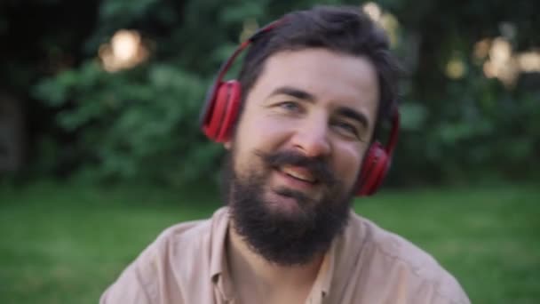 Retrato en la cabeza de un hombre barbudo alegre sonriente y guapo con bigote escuchando música en auriculares sonriendo y cantando. primer plano feliz cara de satisfecho despreocupado caucásico hombre disfrutando de hobby. — Vídeos de Stock