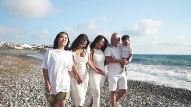 Extended Asian family walking in slow motion on picturesque Mediterranean sea coast talking and laughing. Happy man women and child strolling on vacations at sunset sunshine outdoors. — Stock Video