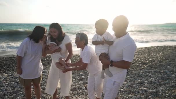 Positiva famiglia multigenerazionale asiatica in piedi alla luce del sole sulla spiaggia turchese del Mar Mediterraneo ridendo parlando al rallentatore. Felice uomini rilassati donne e bambini godendo vacanze all'aria aperta. — Video Stock