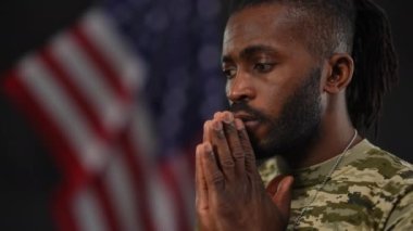 Afrika kökenli üzgün bir Amerikan askerinin el ele tutuşmayı düşünmesi. Siyah arka planda Amerikan bayrağı taşıyan düşünceli genç erkek askerin portresi..