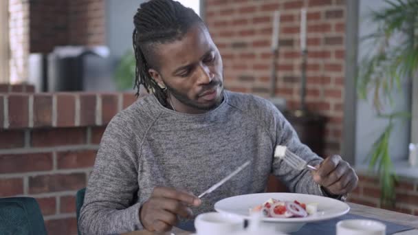 Confident handsome African American man eating feta cheese from Greek salad sitting in luxurious restaurant. Portrait of male customer tasting delicious food indoors. Slow motion. — Stock Video