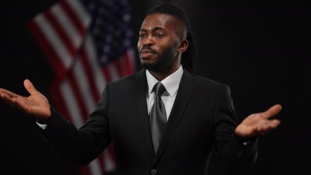 Pozitif Afro-Amerikalı erkek politikacı alkışlıyor. İlgi için teşekkür ediyor ve başparmaklarını kaldırıyor. Sahnede kendine güveni tam yakışıklı bir diplomat portresi ve arkasında ABD bayrağı. — Stok video