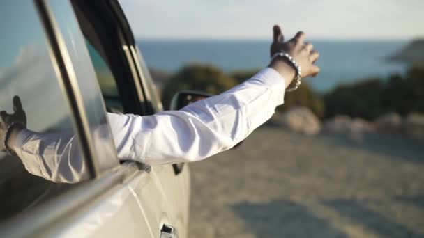 Mužská afroamerická ruka trčící z okna auta na pozadí malebného tyrkysového Středozemního moře. Nerozpoznatelný mladý turista obdivující krajinu při západu slunce. Zpomalený pohyb. — Stock video