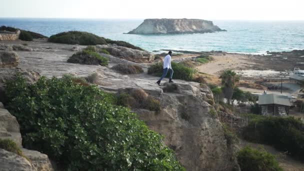Ακραίο πλάνο του Αφροαμερικανού τουρίστα που απλώνει τα χέρια του πάνω σε βράχια στις μπλε ακτές της Μεσογείου. Ευτυχισμένος ενθουσιασμένος νεαρός θαυμάζοντας θαλασσογραφία απολαμβάνοντας αναψυχής σε εξωτερικούς χώρους. — Αρχείο Βίντεο