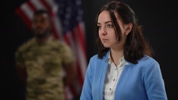 Femme caucasienne enthousiaste parlant et applaudissant avec un soldat afro-américain flou en arrière-plan au drapeau des États-Unis. Portrait du porte-parole militaire présentant un vétéran courageux lors d'une conférence de presse. — Video