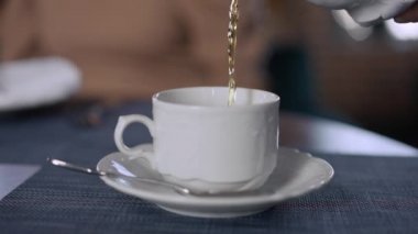 Yakın plan yeşil çay ağır çekimde beyaz bardağa dökülüyor. Restoranda müşteriye servis yapan tanınmamış bir garson. Hizmet sektörü ve eğlence konsepti.