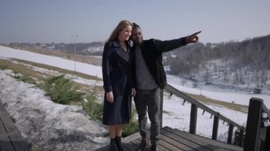 Gülümseyen Afrikalı Amerikalı sevgili adam otelin terasında gün ışığında beyaz bir kadınla konuşuyor. Avrupa 'da kış tatillerinde dinlenen mutlu çiftin geniş açılı portresi..