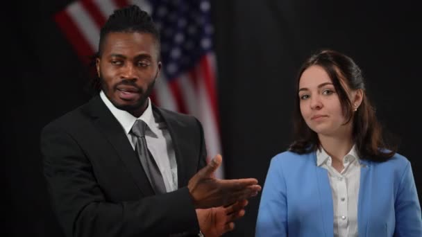 African American male politician giving the floor to Caucasian female spokesperson in camera flashes at press conference. Portrait of confident man and woman talking looking around. — Stock Video