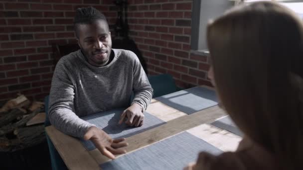 Portrait of loving smiling African American man taking hand of Caucasian woman talking in slow motion sitting at table in restaurant. Happy young boyfriend enjoying dating with girlfriend indoors. — Stock Video